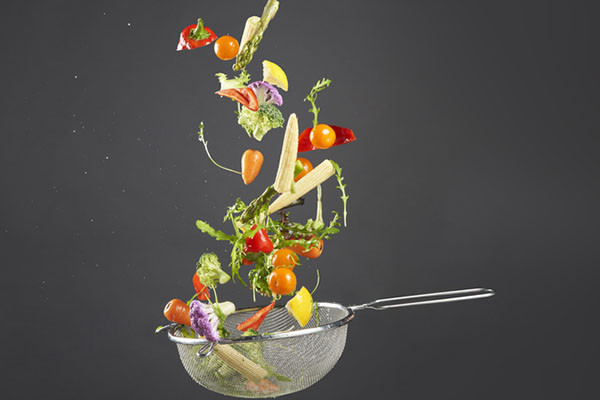 photo of assorted fresh vegetables being tossed in a strainer after being rinsed